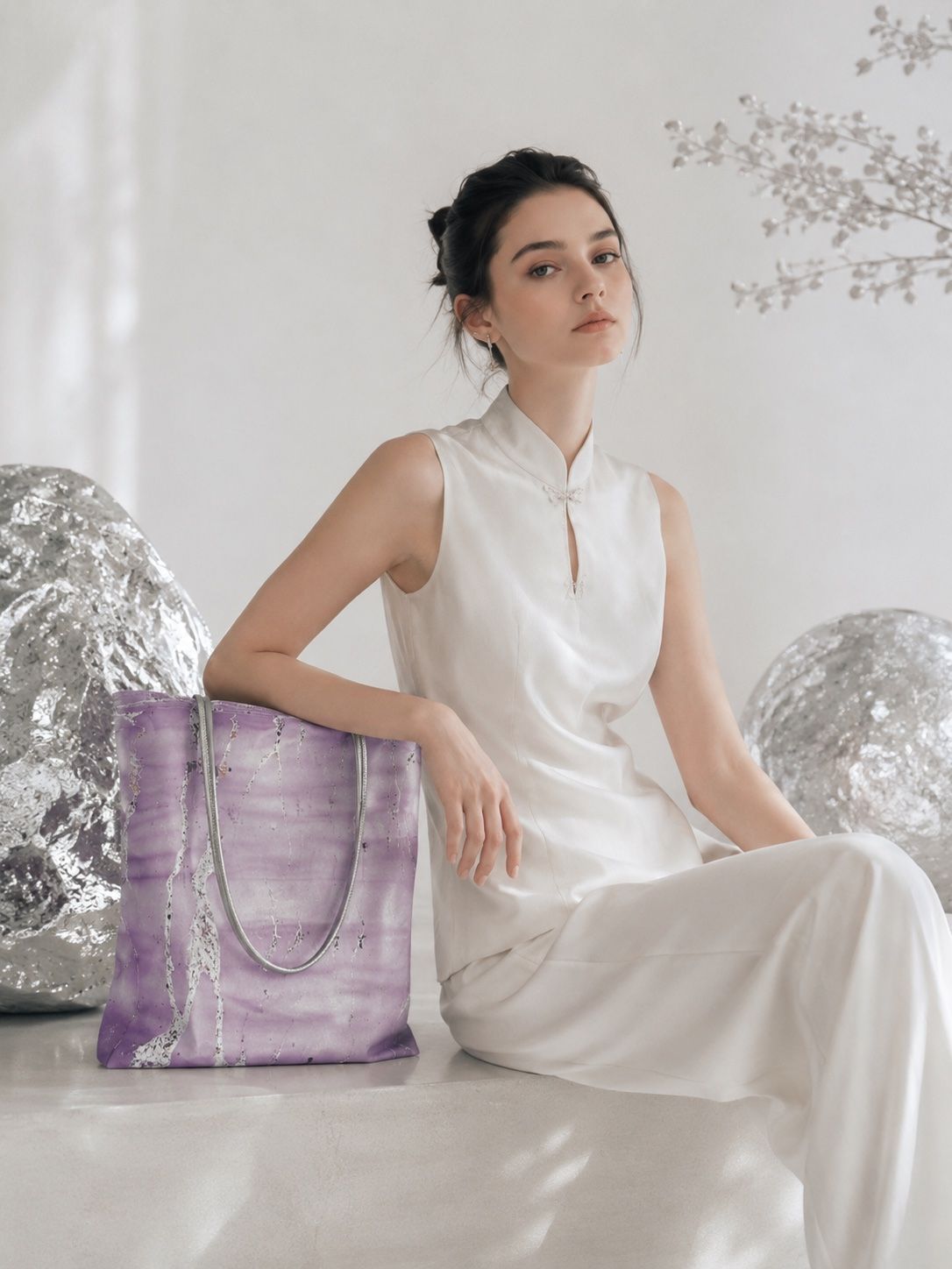 Model in ivory seated beside a one-of-one violet floating-lacquer shoulder bag