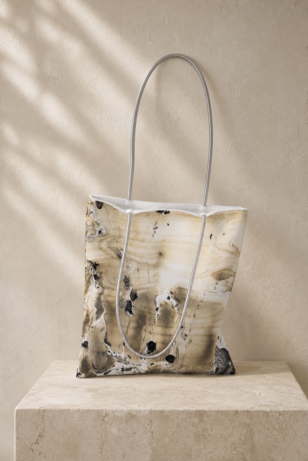 Stone Whisper sand and black velvet shoulder bag on a warm stone plinth